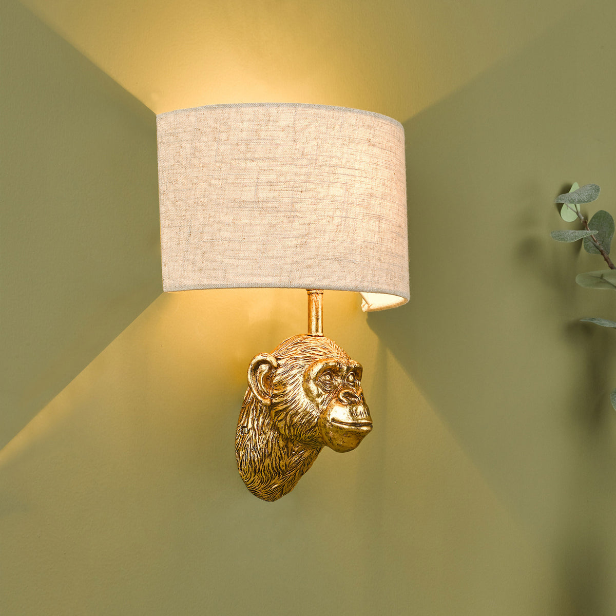 Golden monkey head wall sconce with a light beige fabric shade, casting warm light on a green wall.