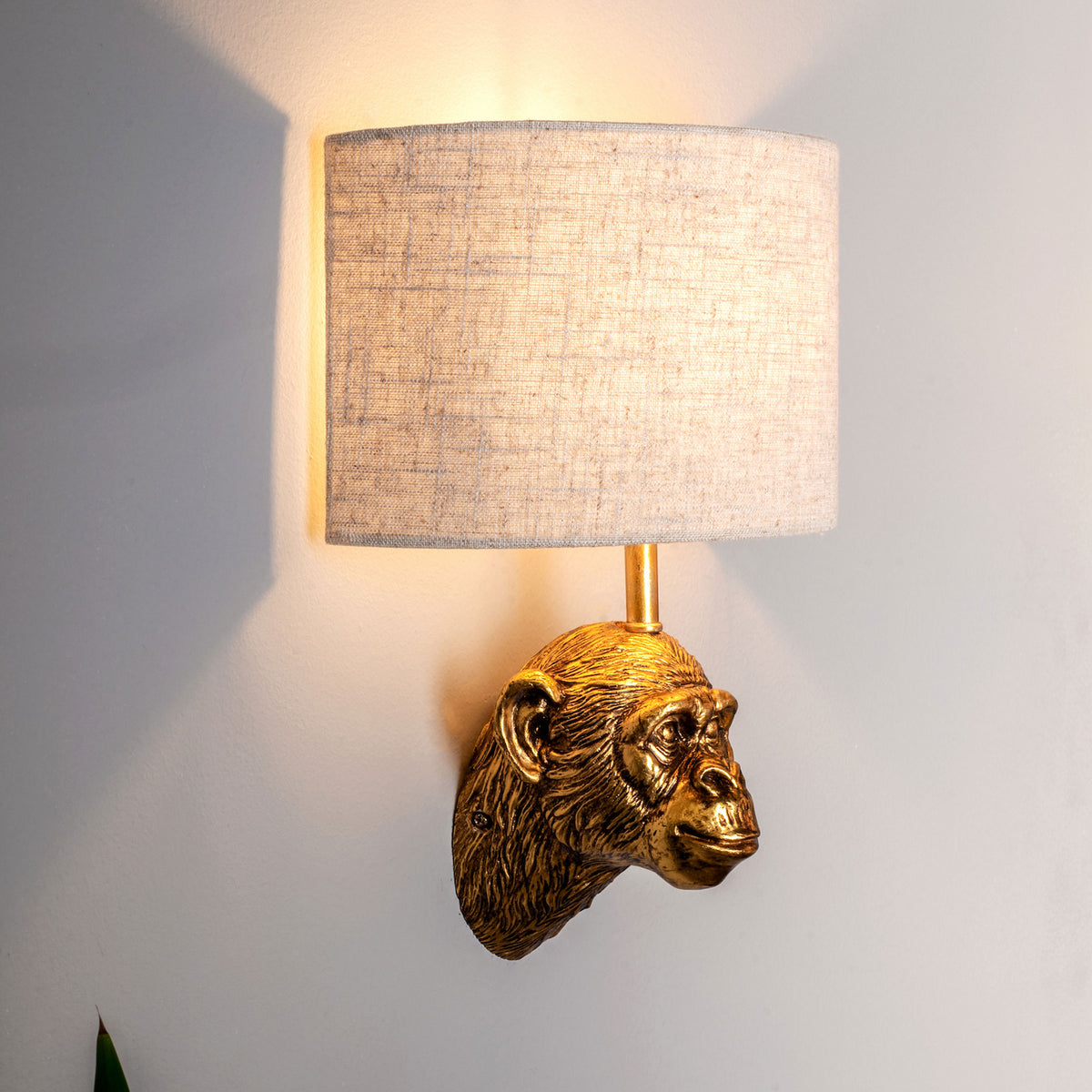 Golden monkey head wall sconce with a light beige fabric shade, casting a warm glow on a white wall.