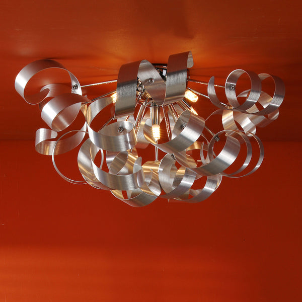 Modern ceiling light with brushed silver metal ribbons and exposed bulbs against an orange ceiling.