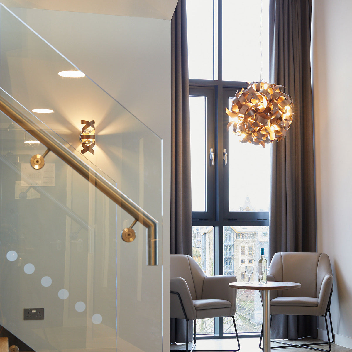 Modern interior with glass staircase, wall sconces, and a seating area with a unique pendant light.