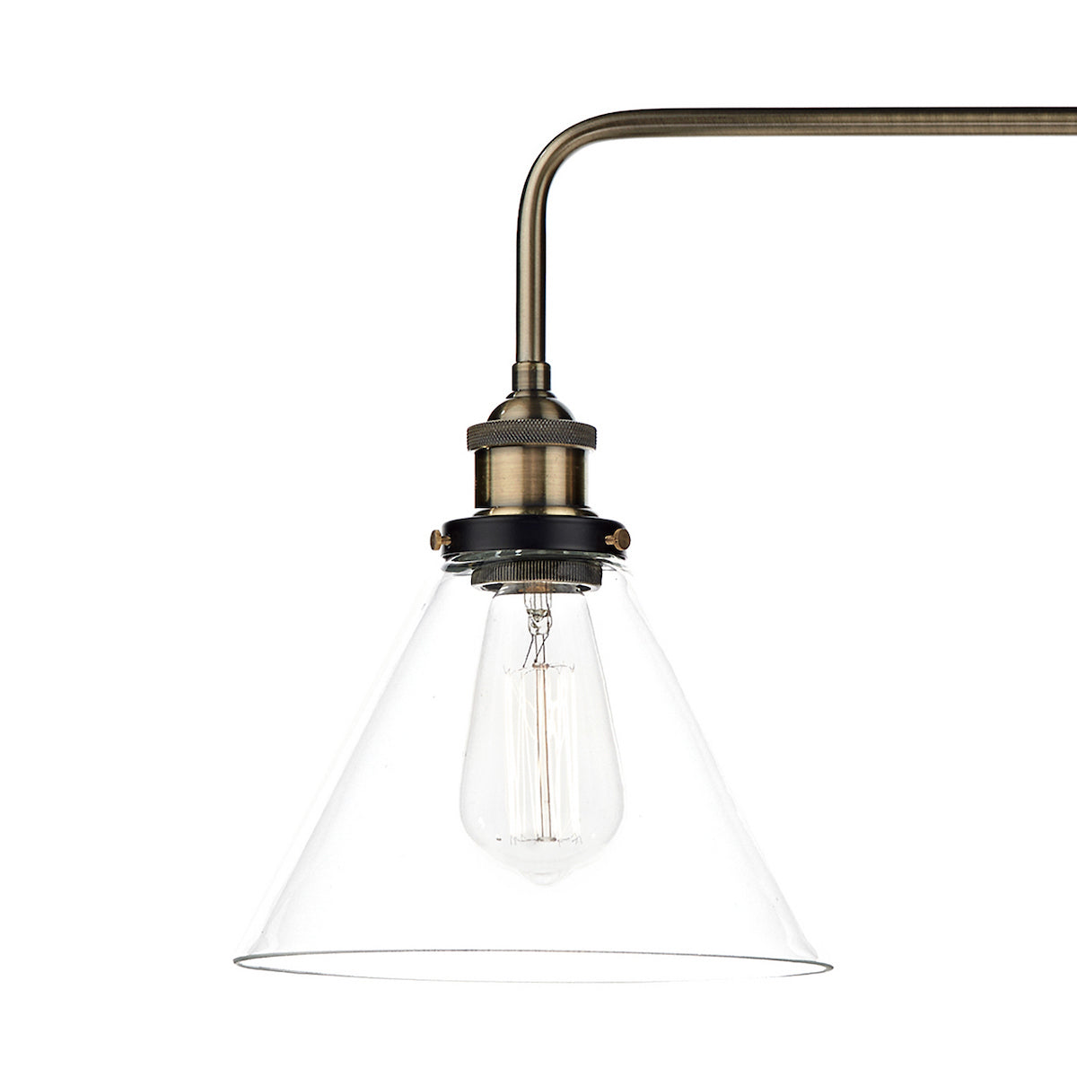 Close-up of a brass light fixture with a clear, conical glass shade and an Edison bulb.