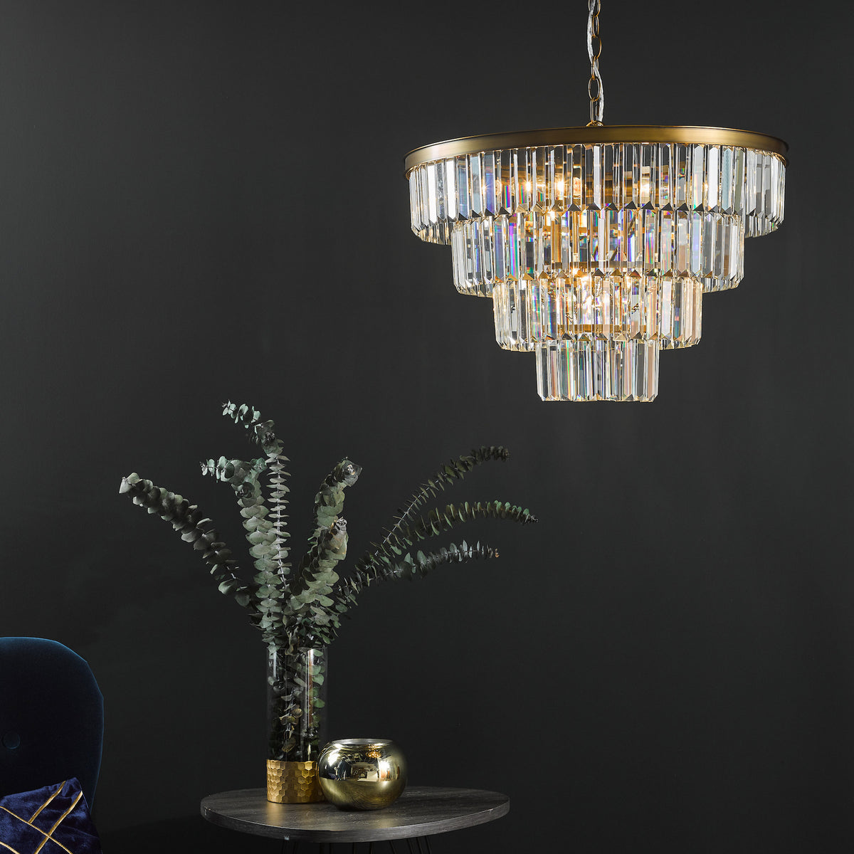 Tiered crystal chandelier with gold accents, illuminating a dark room with a plant in a vase on a side table