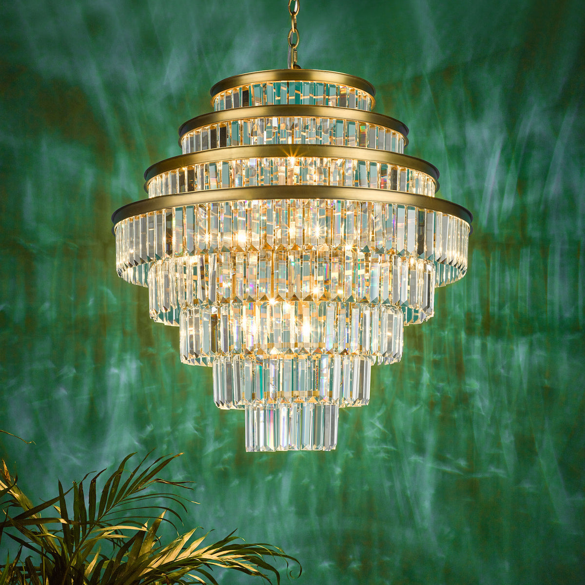 Tiered crystal chandelier with gold accents against a green wall