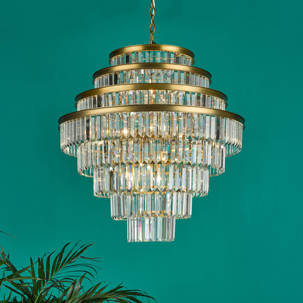 Tiered crystal chandelier with brass accents against a teal background