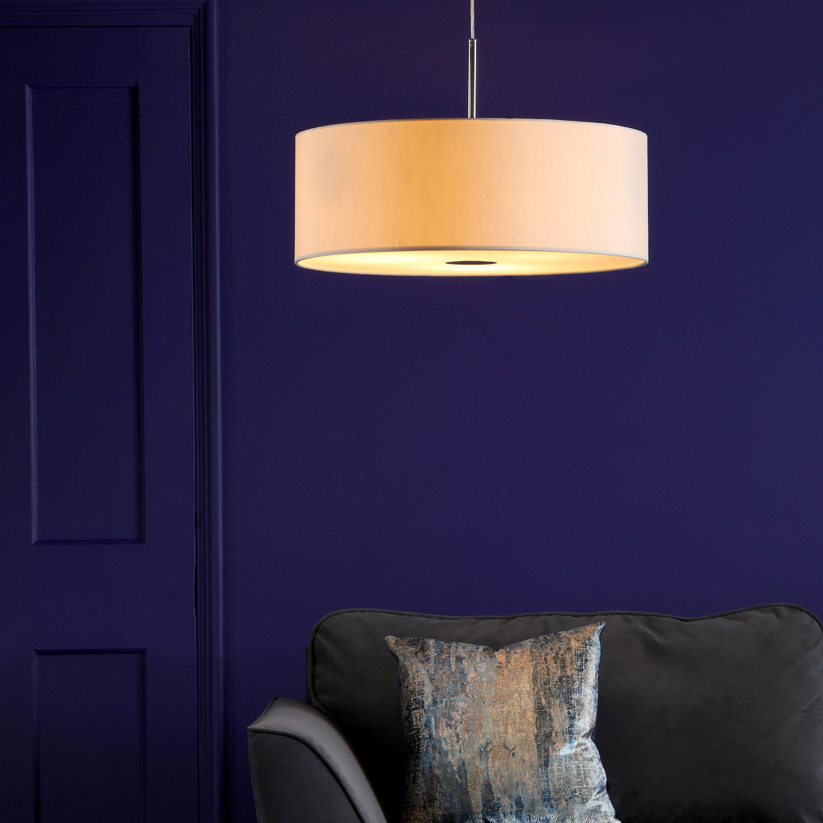 A cream drum pendant light hangs above a dark gray sofa with a textured blue and gold pillow.