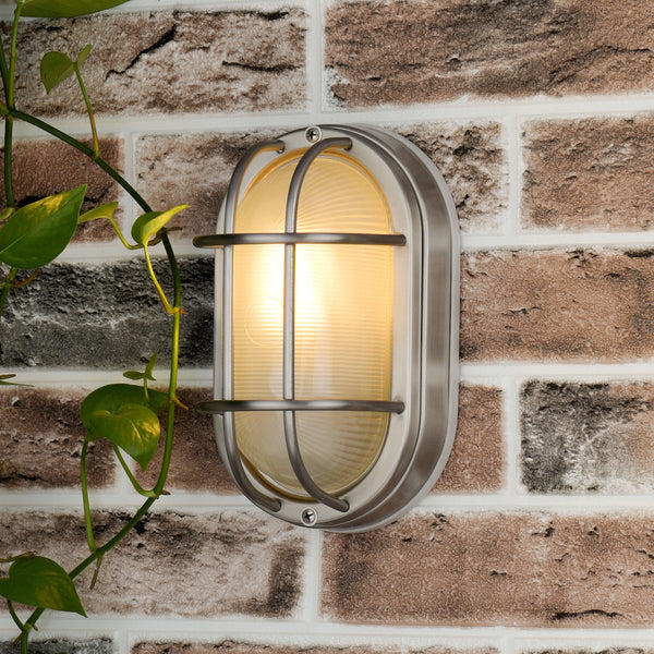 An oval outdoor wall light with a brushed nickel finish and ribbed glass, mounted on a brick wall.