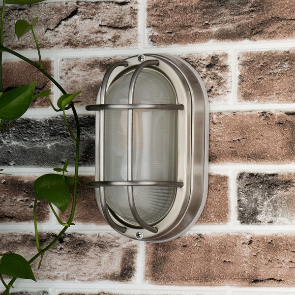 Oval brushed nickel outdoor light fixture on a brick wall with a green vine.