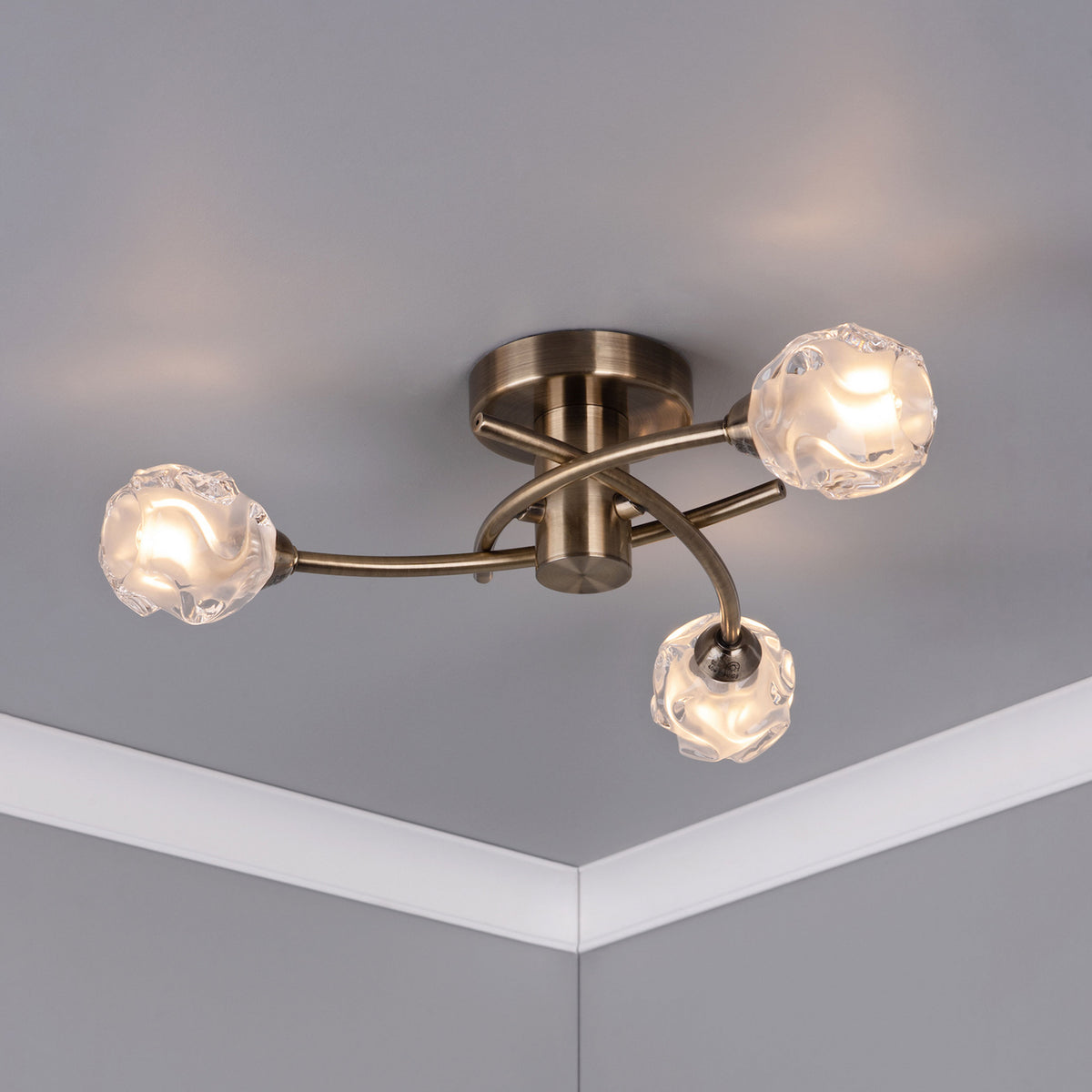 Bronze ceiling light with three twisted arms, each holding a clear, textured glass shade with a glowing bulb.