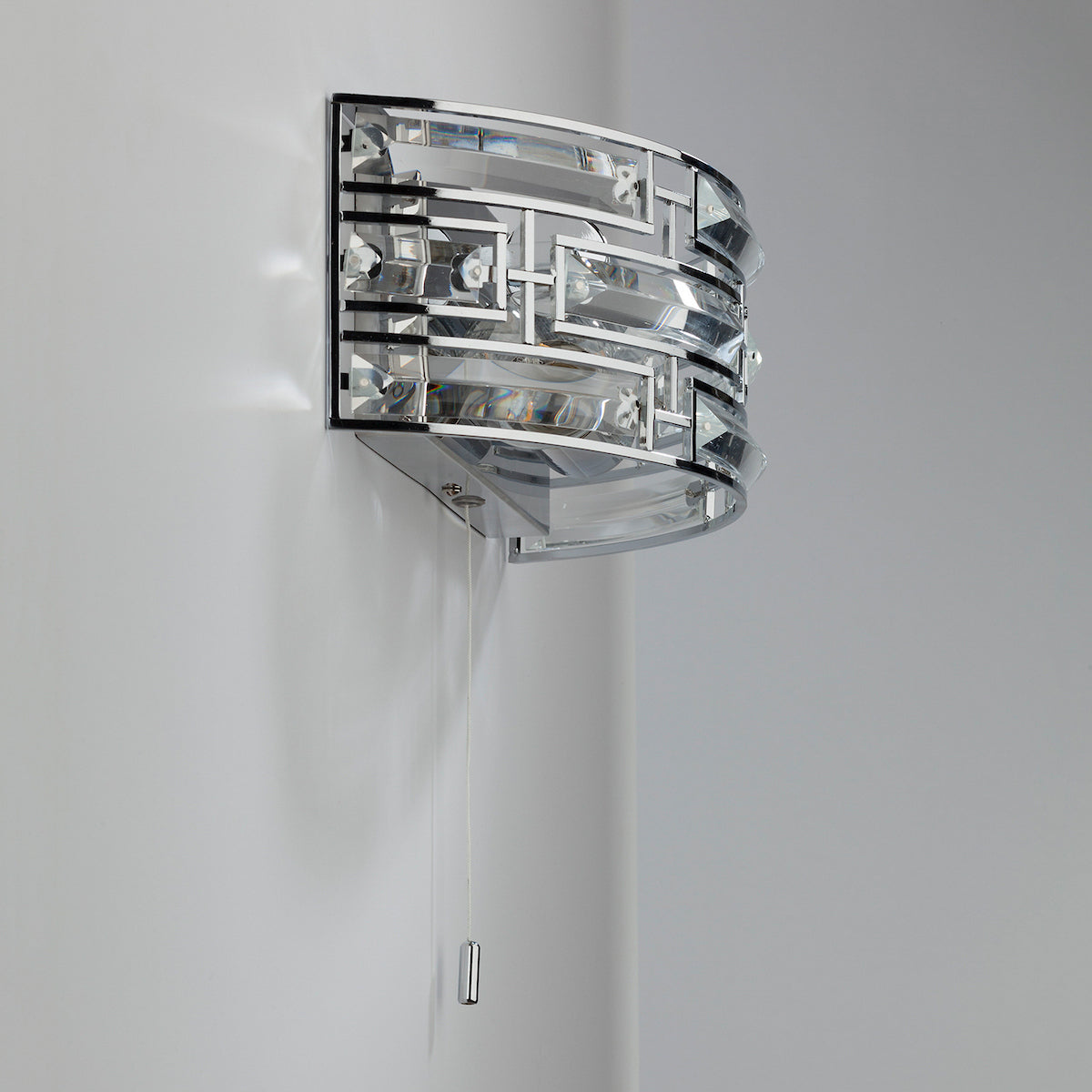 A chrome and glass wall sconce with a pull chain hangs on a white wall.