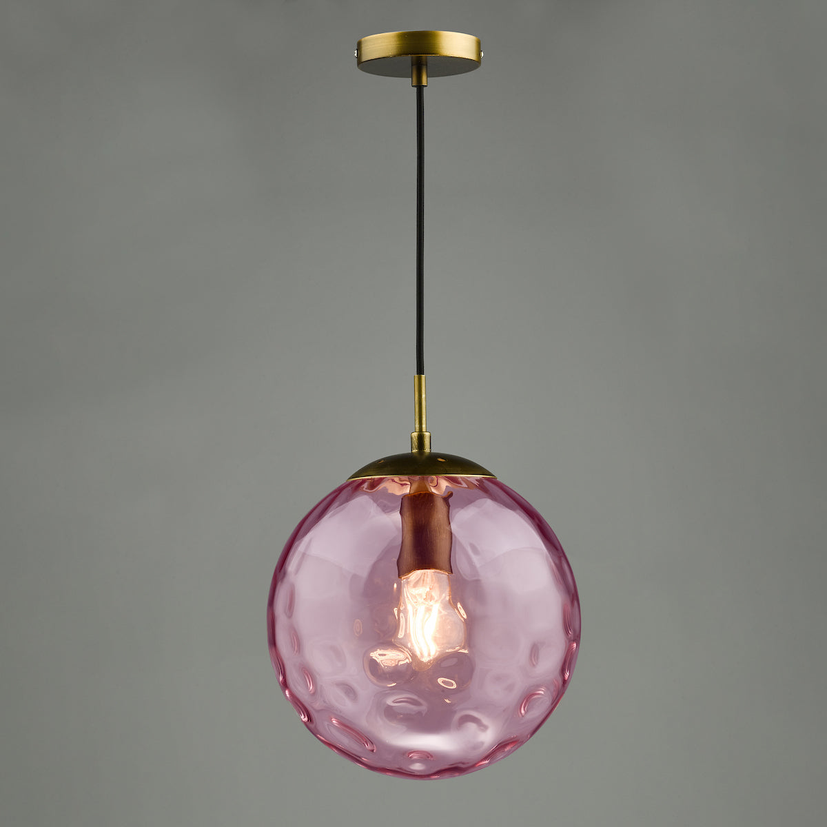 Pink textured glass pendant light with a brass fixture and exposed bulb.