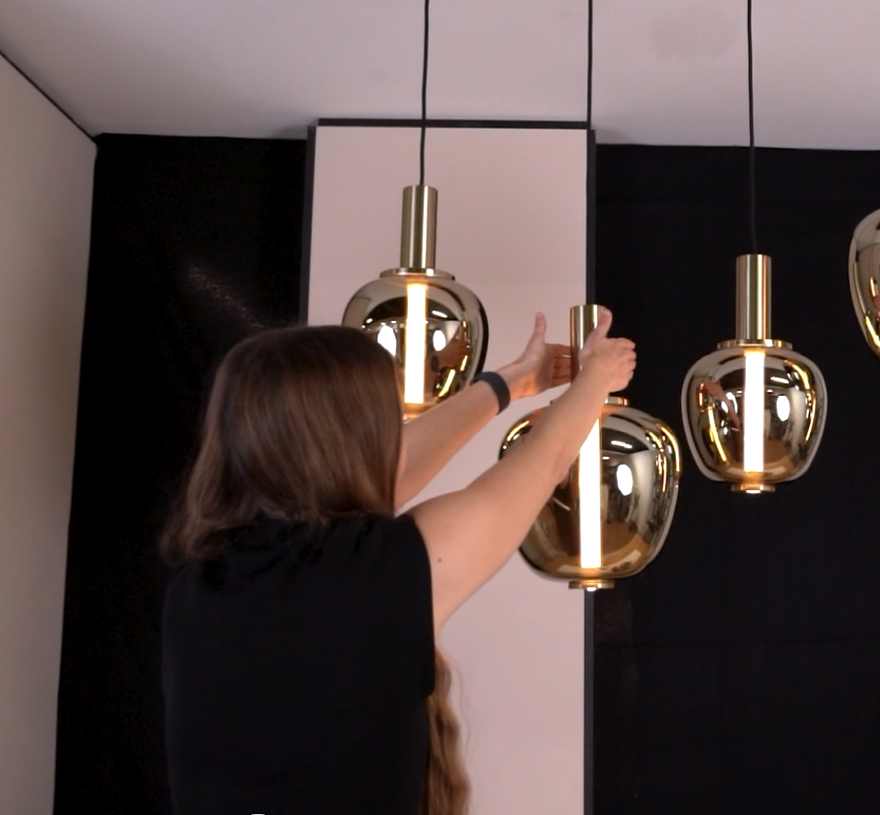 Woman adjusting a gold pendant light fixture in a room with black and white walls.