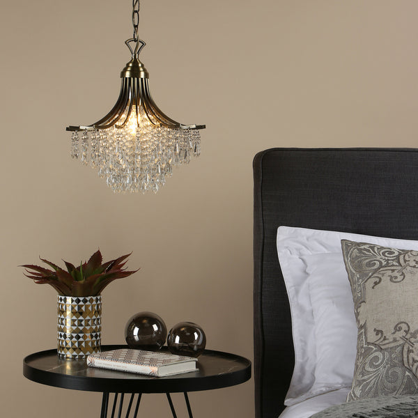 A brass chandelier with crystal drops hangs above a black marble side table with a plant, two glass orbs, and a book.