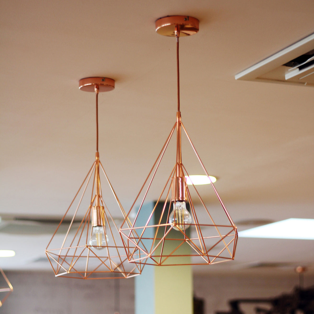 Two modern copper geometric pendant lights with exposed bulbs hang from a light-colored ceiling.
