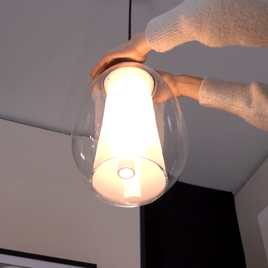 Hands adjusting a clear glass pendant light with a white inner diffuser