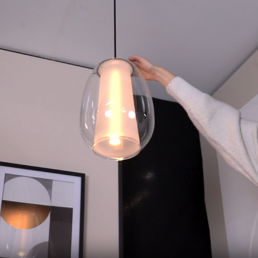 Hand adjusting a modern glass pendant light with a frosted inner cylinder and warm glow