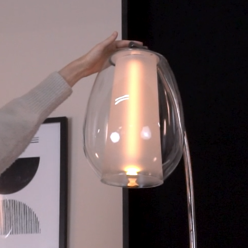 Hand adjusting a modern floor lamp with a clear glass shade and an illuminated frosted inner cylinder
