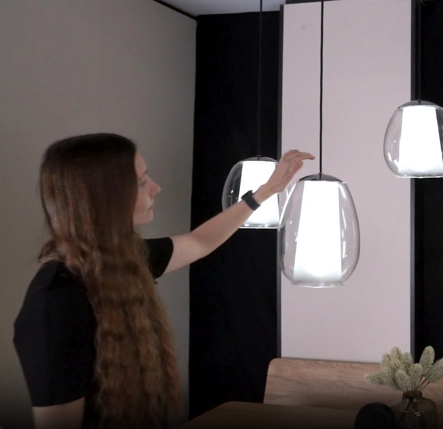 Woman adjusting a hanging glass pendant light with a white inner shade
