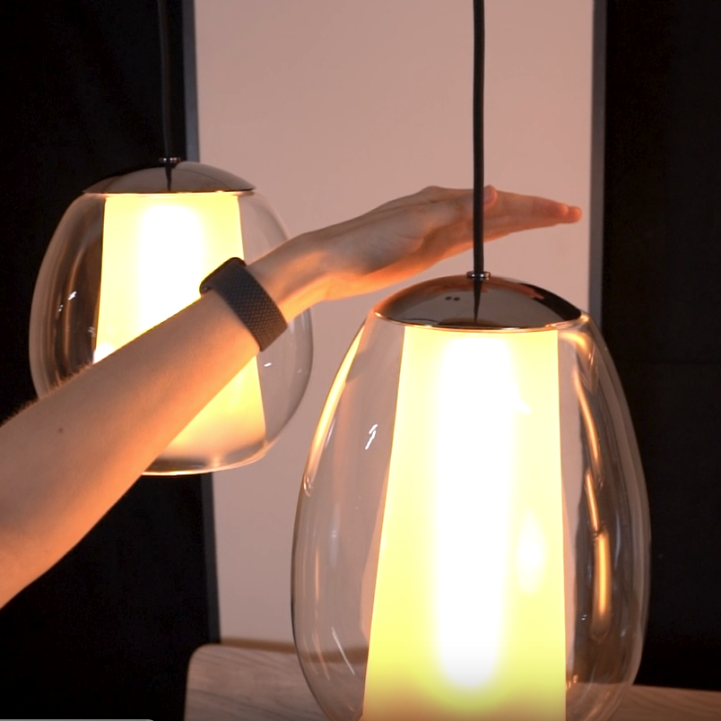 Hand adjusting a clear glass pendant light with a glowing yellow interior