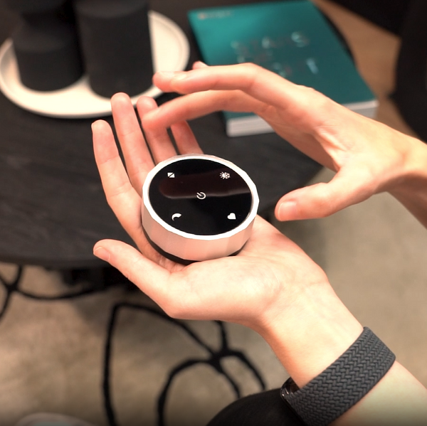Hand holding a circular smart home device with a black screen and white icons