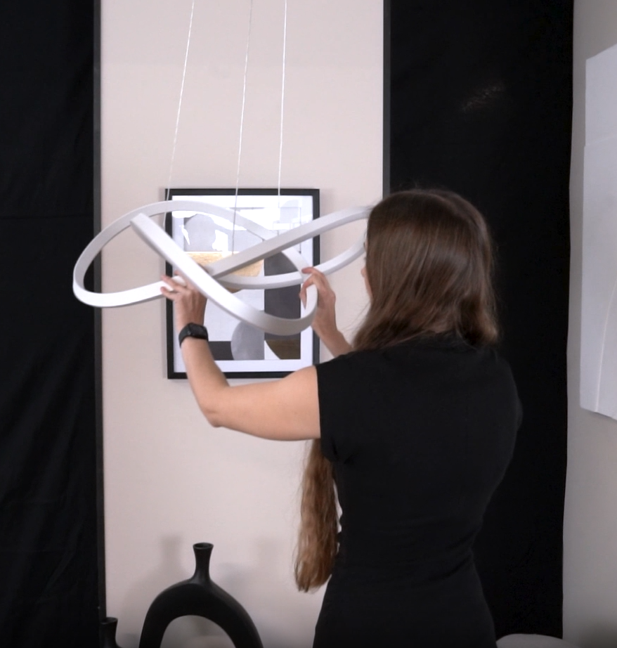 Woman adjusting a modern white pendant light fixture with intertwined rings
