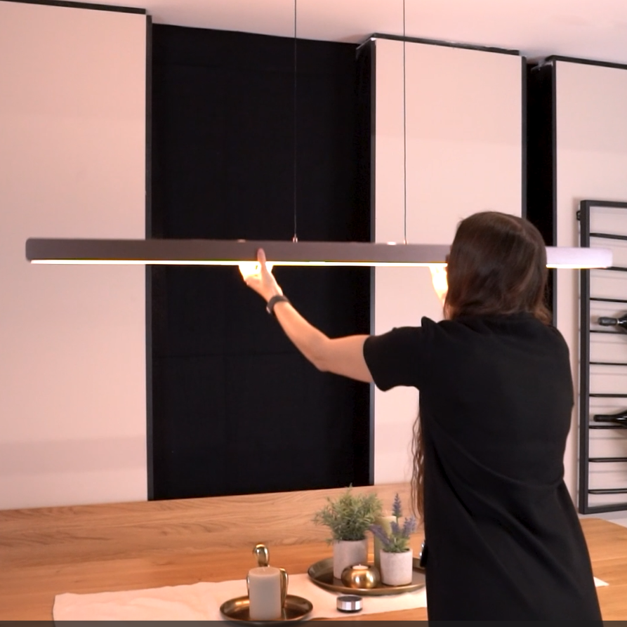 Woman adjusting a linear pendant light fixture above a wooden table
