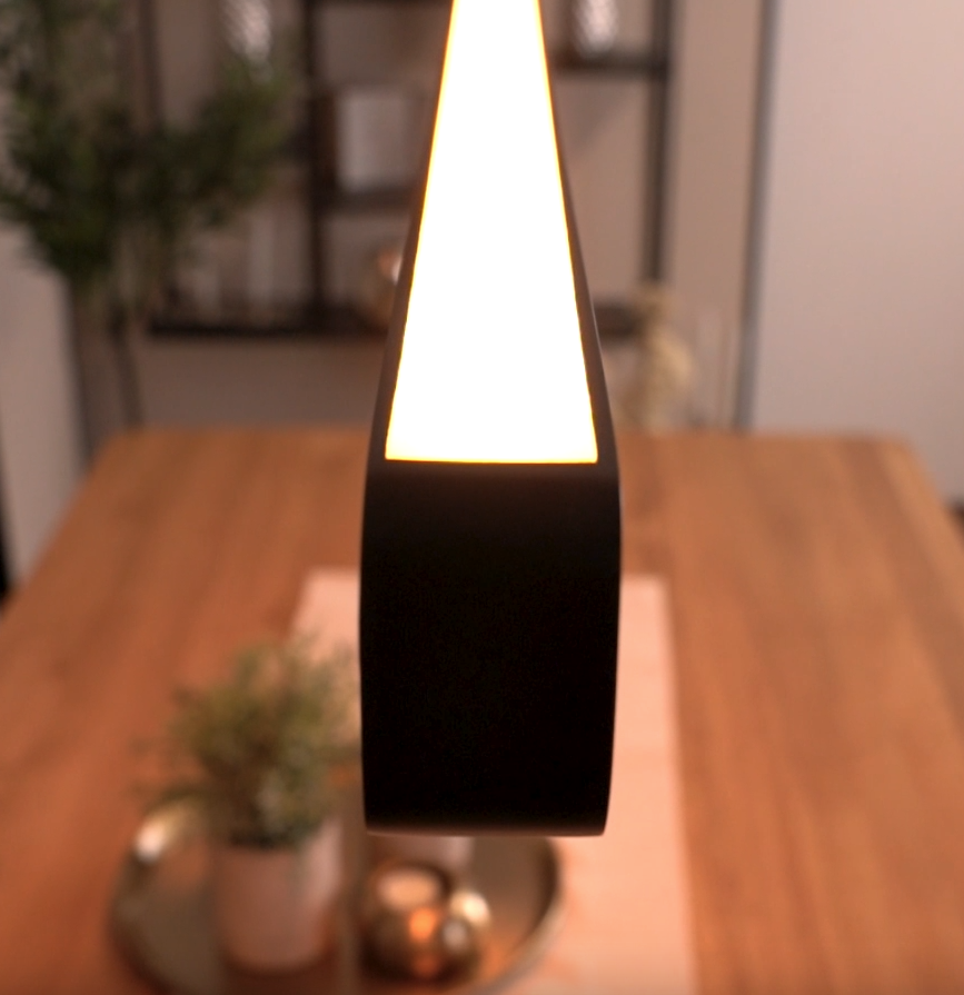 Black pendant light with a bright white glow hanging above a wooden table
