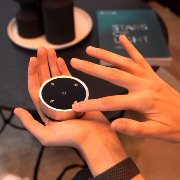 Hand holding a small, round, silver device with a black top and white icons
