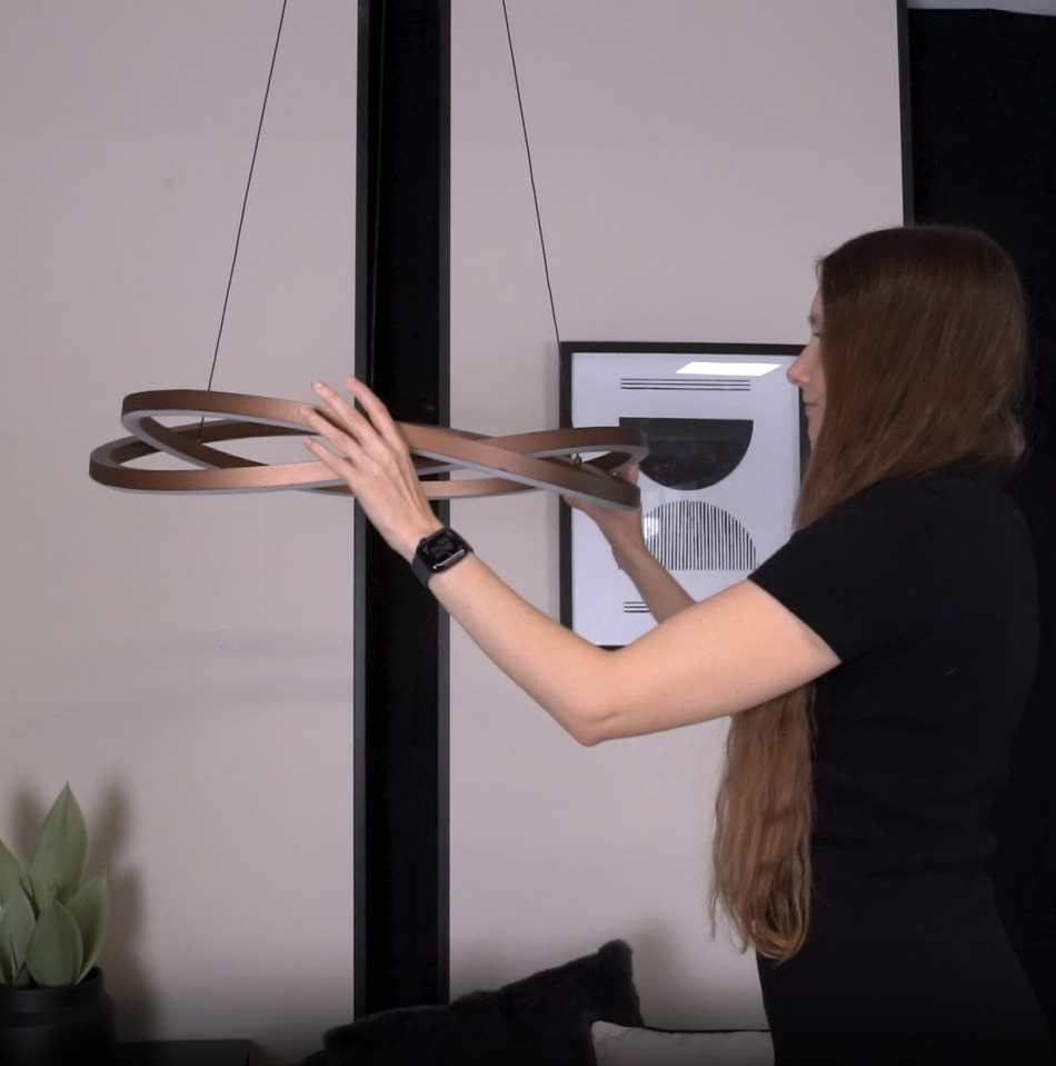 Woman adjusting a modern bronze-colored LED chandelier with intertwined rings