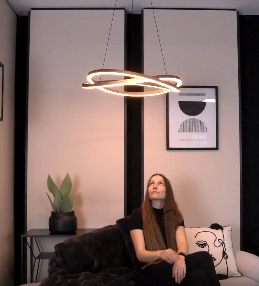 Woman on sofa looking up at a modern, illuminated, wavy chandelier