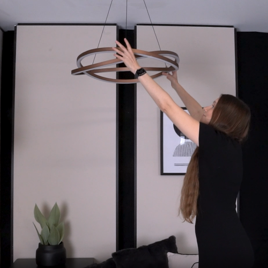 Woman in black dress adjusting a modern circular chandelier with wood and white accents