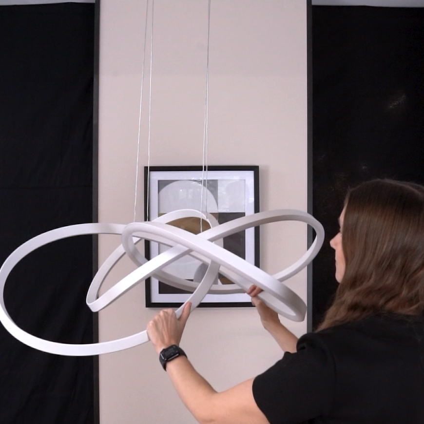 Woman adjusting a modern white pendant light fixture with intertwined rings