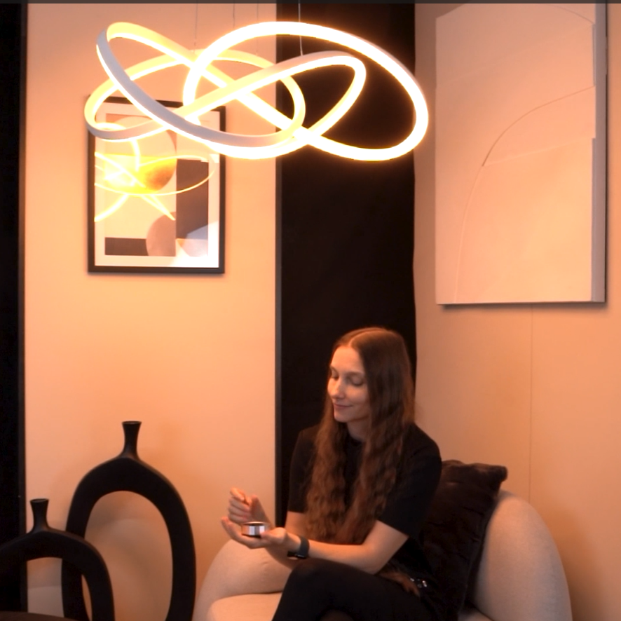 Woman holding a small round object, sitting on a sofa under a modern circular light fixture