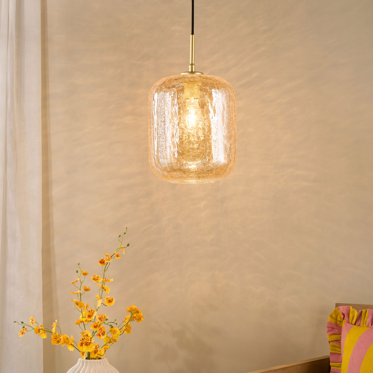 Amber glass pendant light with a textured surface, illuminating a neutral wall above yellow flowers in a white vase