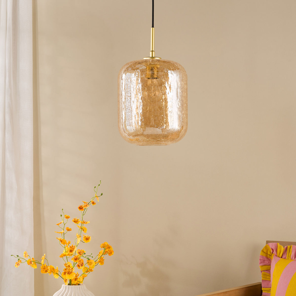 Amber glass pendant light with a brass fixture, above a white vase with yellow orchids