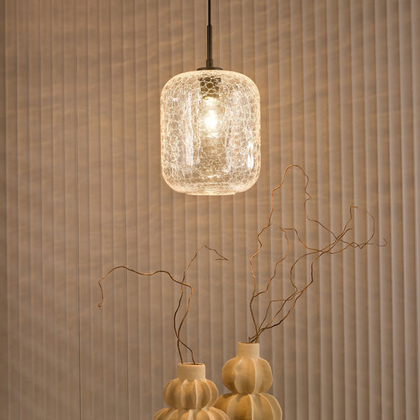 Cracked glass pendant light illuminates two decorative vases with dried branches against a textured wall