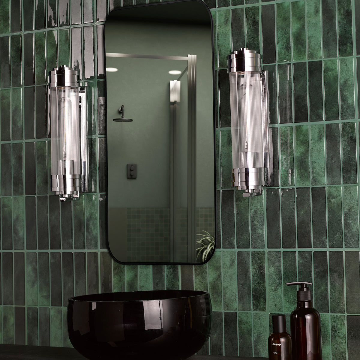 Bathroom with dark green subway tiles, a black mirror, two cylindrical wall lights, and a black basin