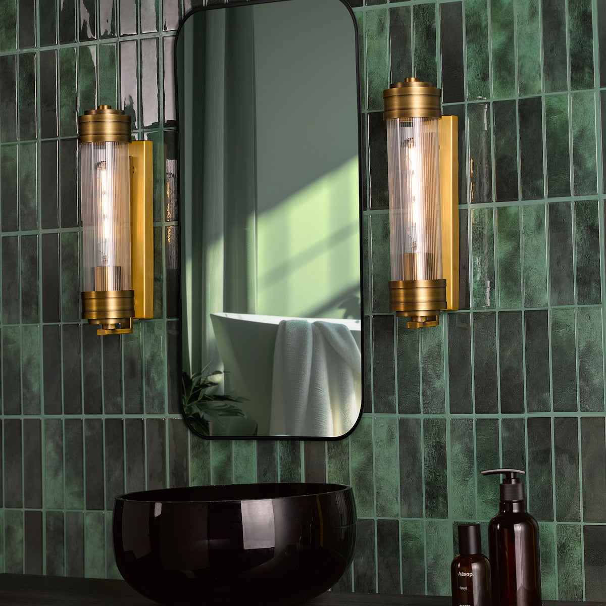 Bathroom with dark green subway tiles, a black mirror, two gold and glass wall sconces, and a black sink