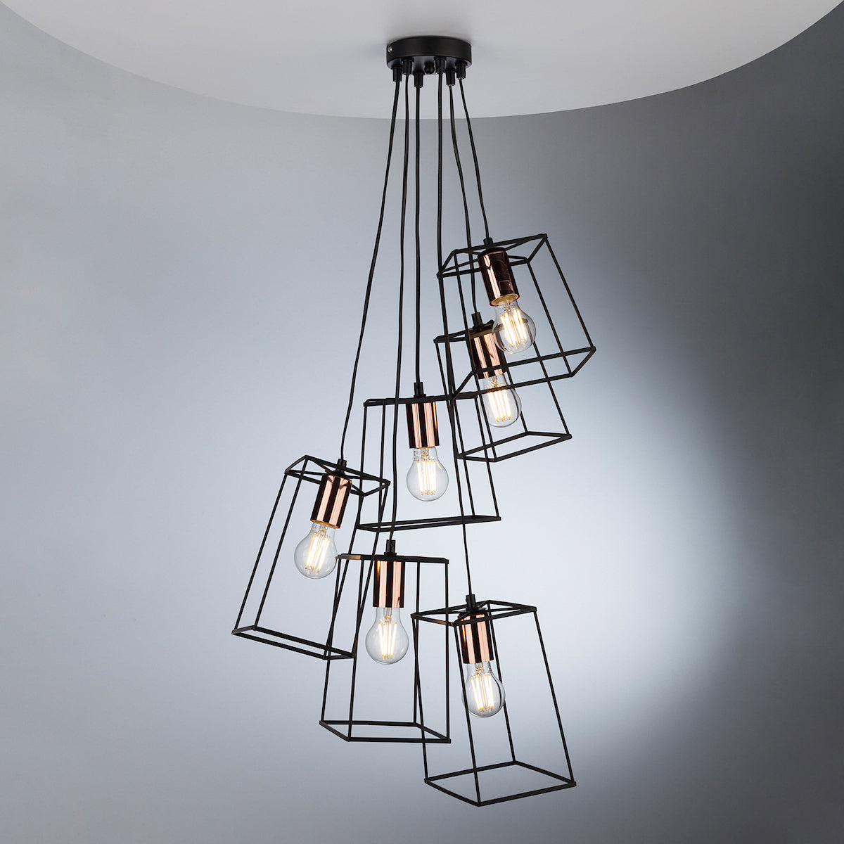 Modern chandelier with six exposed bulbs in black geometric cages and copper accents.