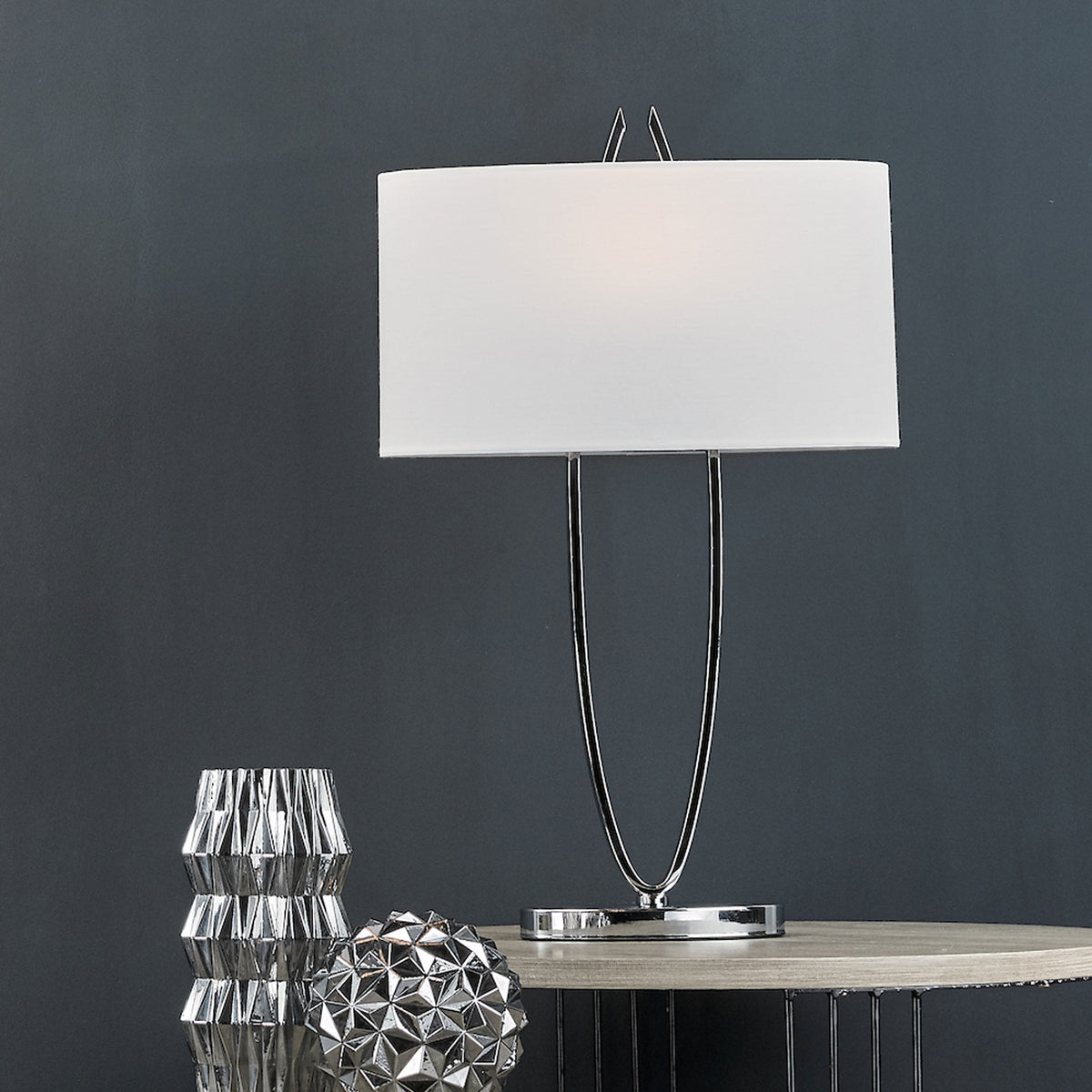 Modern table lamp with a white rectangular shade and chrome base, next to two silver decorative objects.