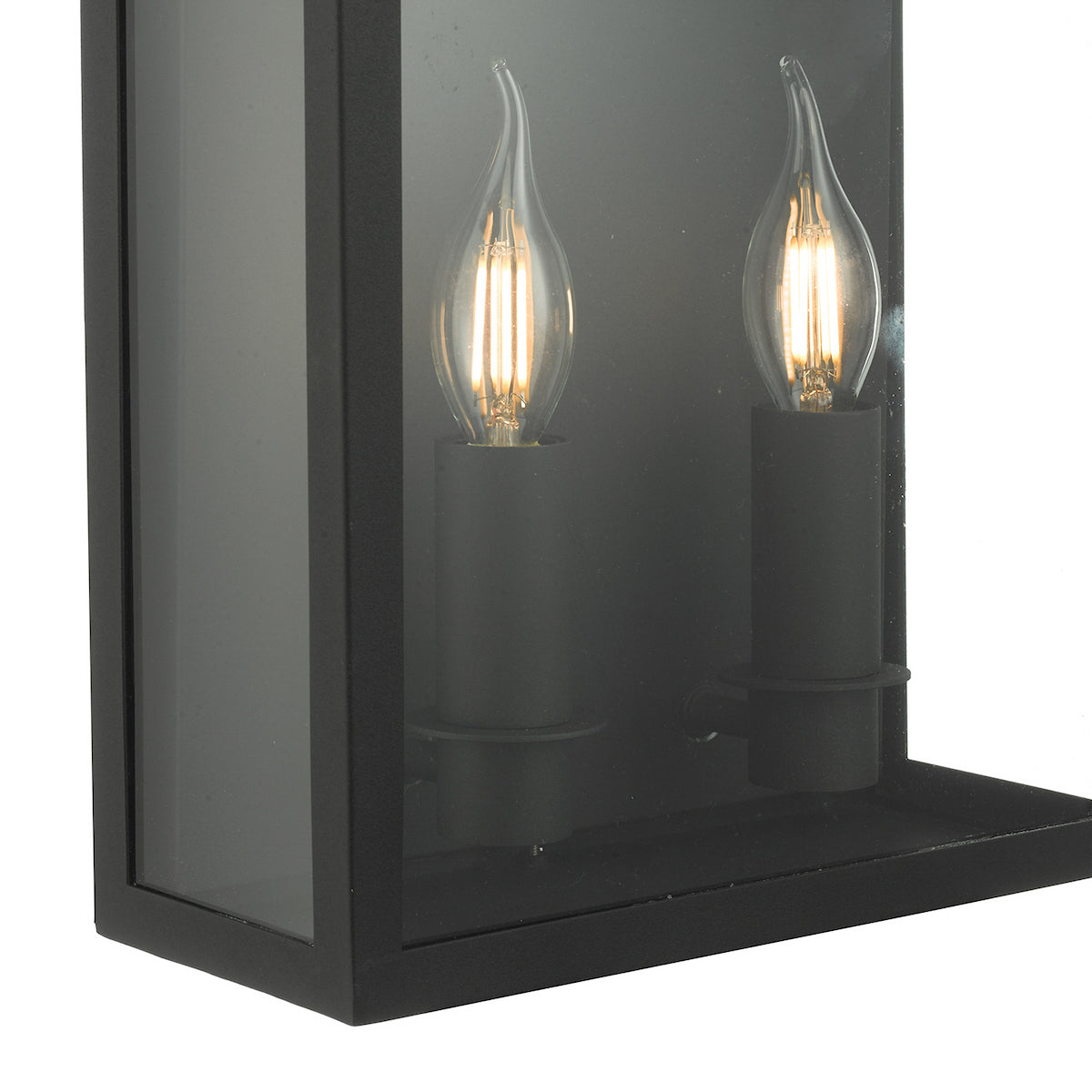 Close-up of a black outdoor wall lantern with two lit, clear, flame-tip bulbs.