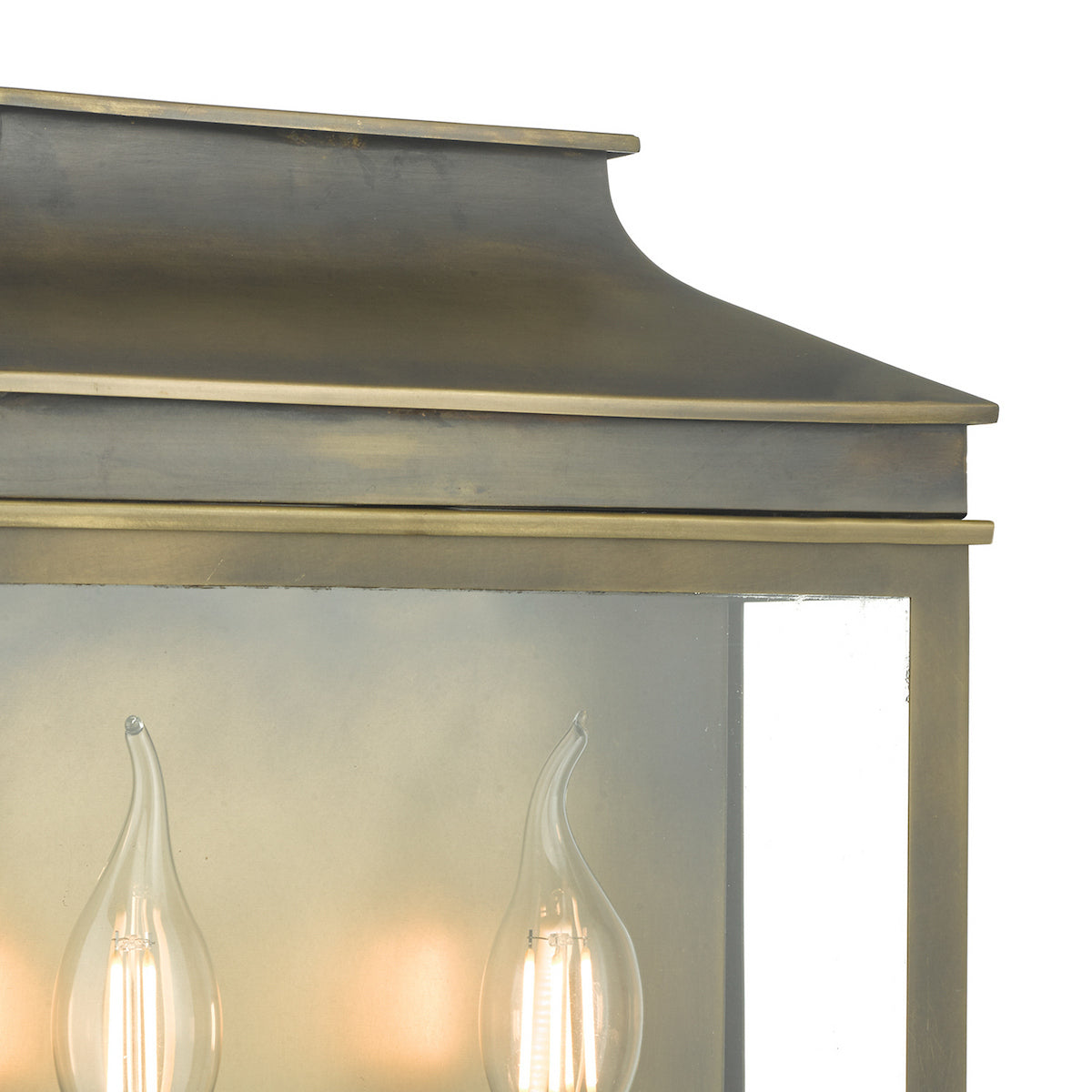 Close-up of a bronze outdoor lantern with two lit, clear, flame-tip light bulbs inside.