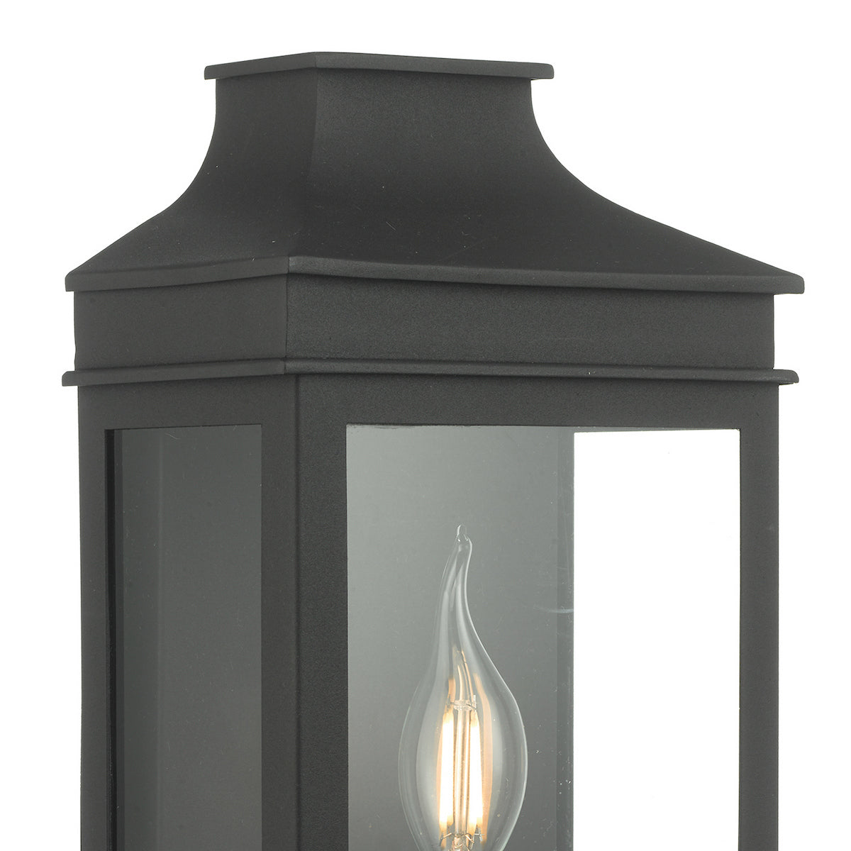 Close-up of a black outdoor wall lantern with a clear glass panel and a flickering flame-tip bulb.