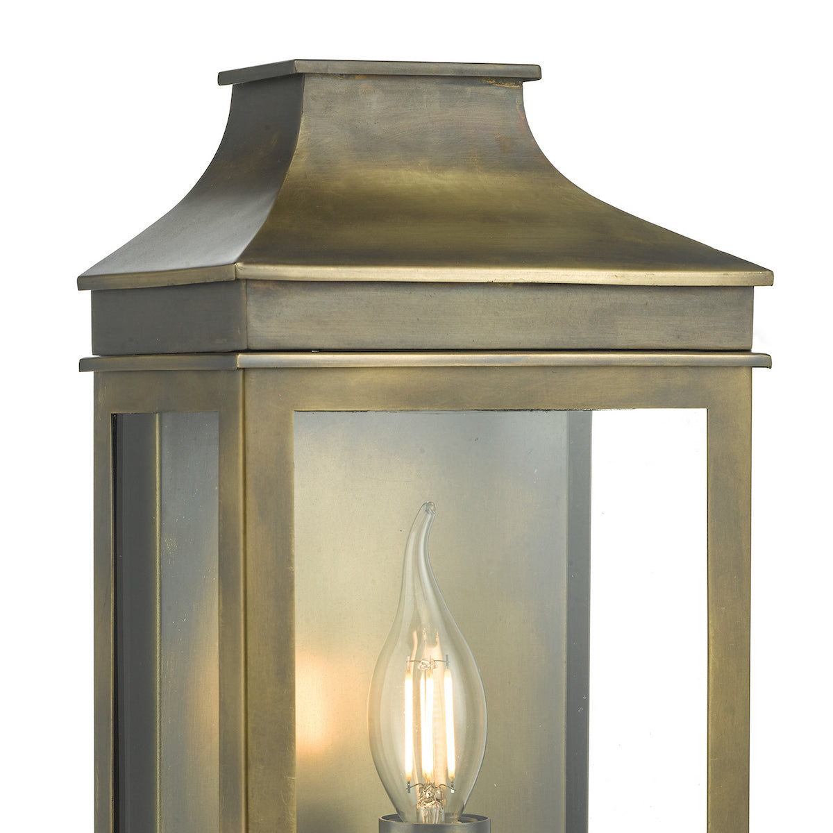 Close-up of a brass outdoor lantern with a lit, flame-shaped LED bulb inside.