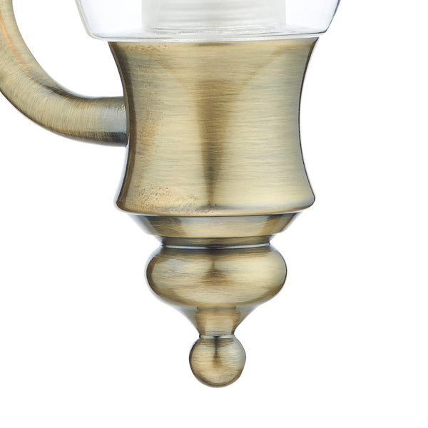 Close-up of a brushed brass light fixture with a glass shade and decorative finial.
