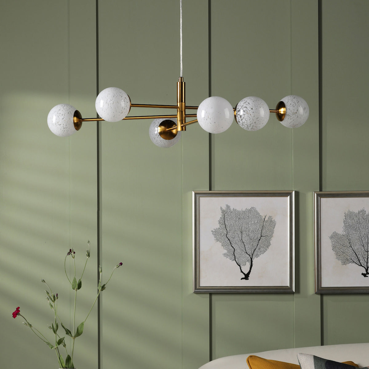 Modern gold chandelier with six white speckled globe lights in a room with green paneled walls.