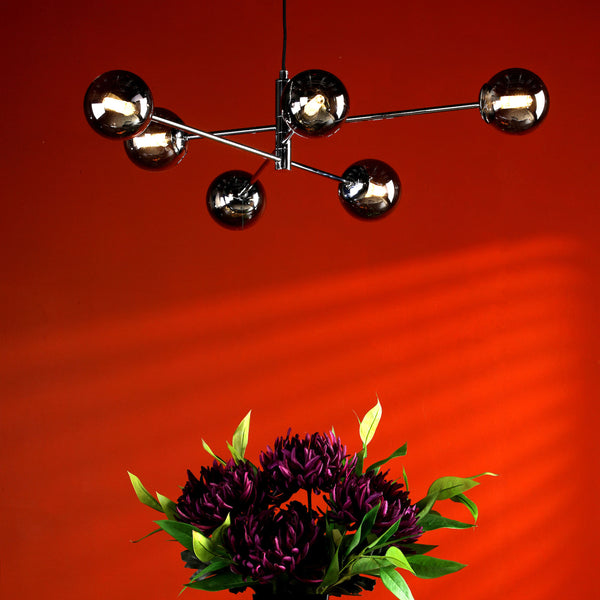 Modern chandelier with six spherical lights and a bouquet of purple flowers against a red wall.