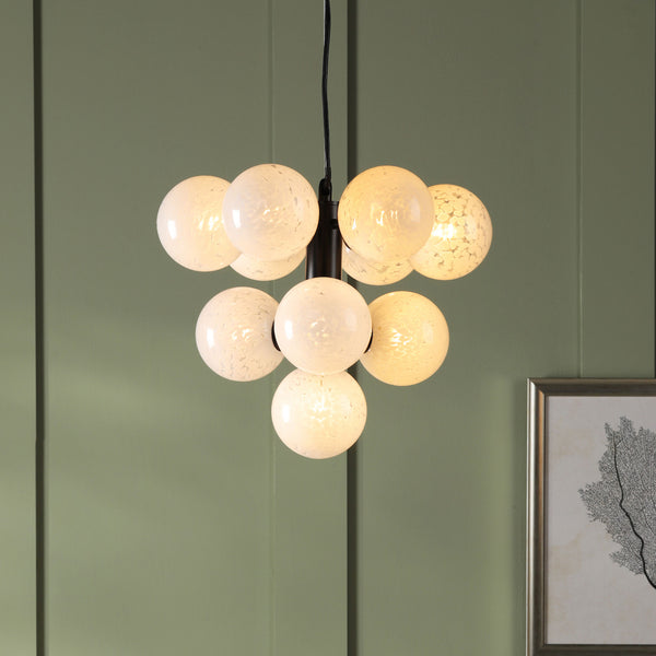 Modern chandelier with eight frosted glass globes, some lit, hanging against a green paneled wall with framed art.