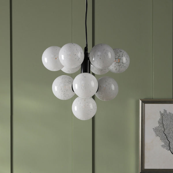 Modern chandelier with nine white speckled glass globes, hanging against a sage green wall.