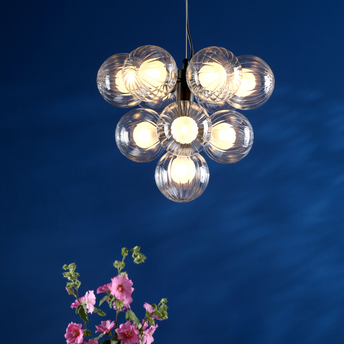 A modern chandelier with seven clear, textured glass globes, each illuminated, against a deep blue wall.