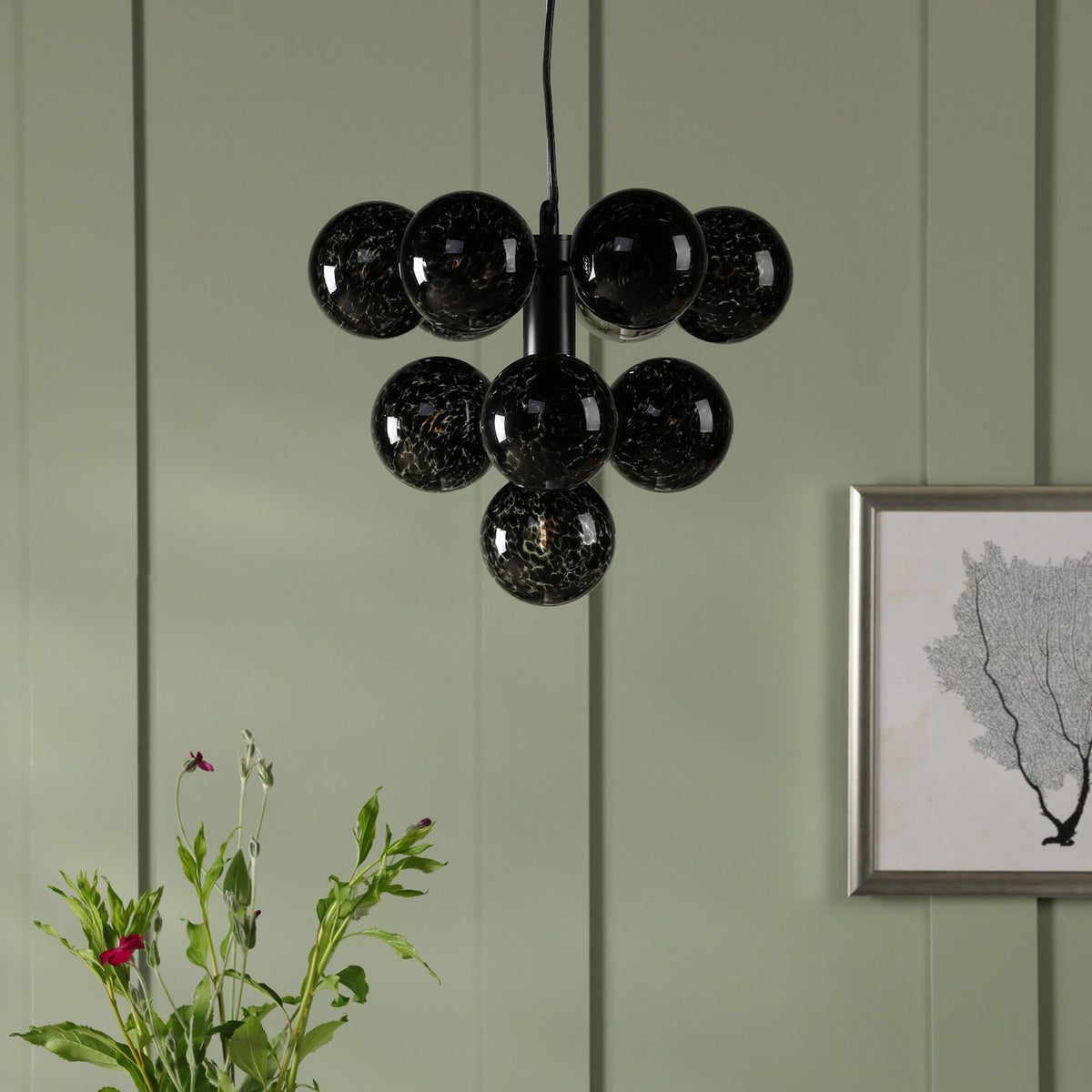 Black glass chandelier with seven round globes, against a sage green paneled wall with a framed print